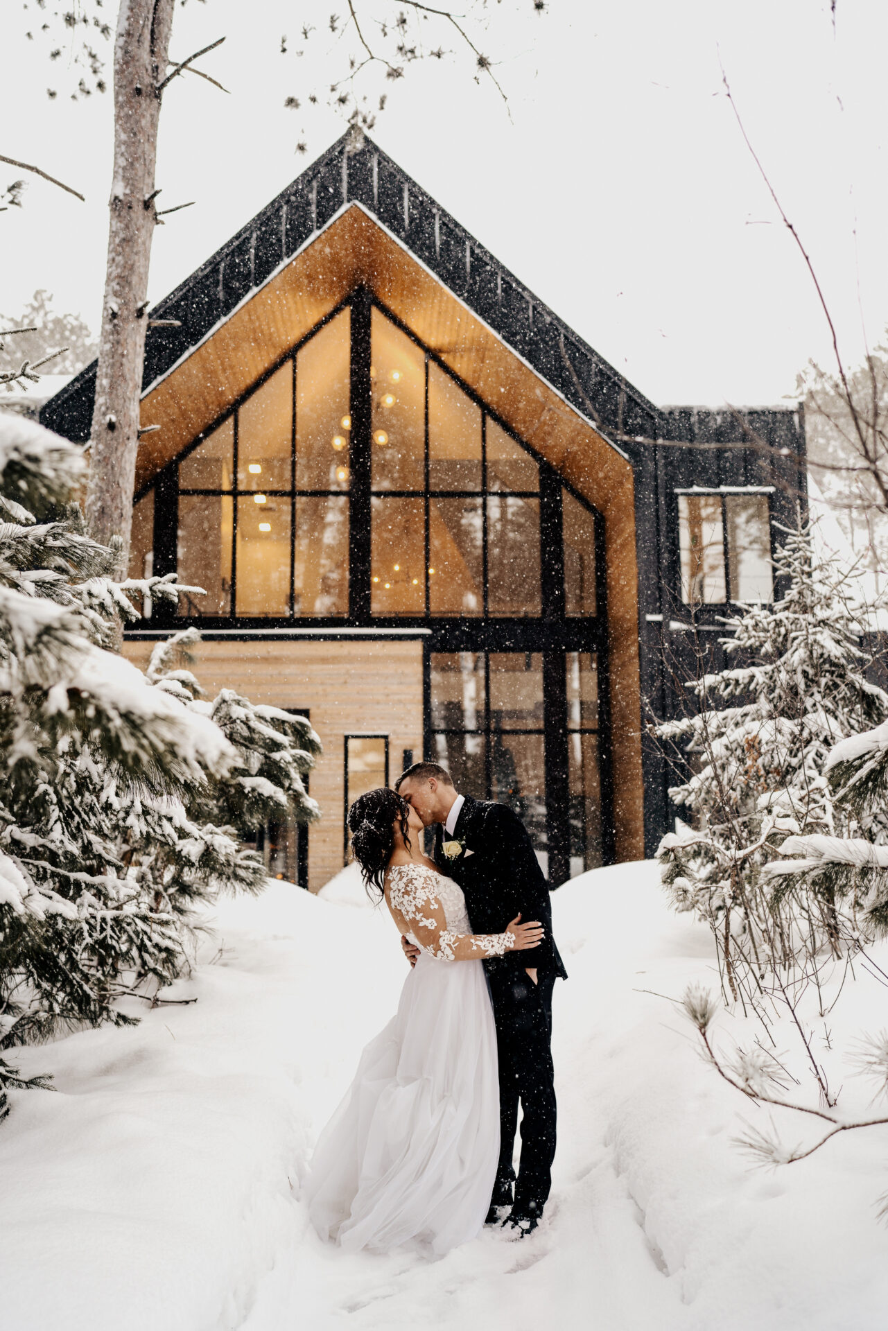 Bride and Groom taking snowy couple portraits in front of Pinewood Weddings & Events Venue in Minnesota during the winter