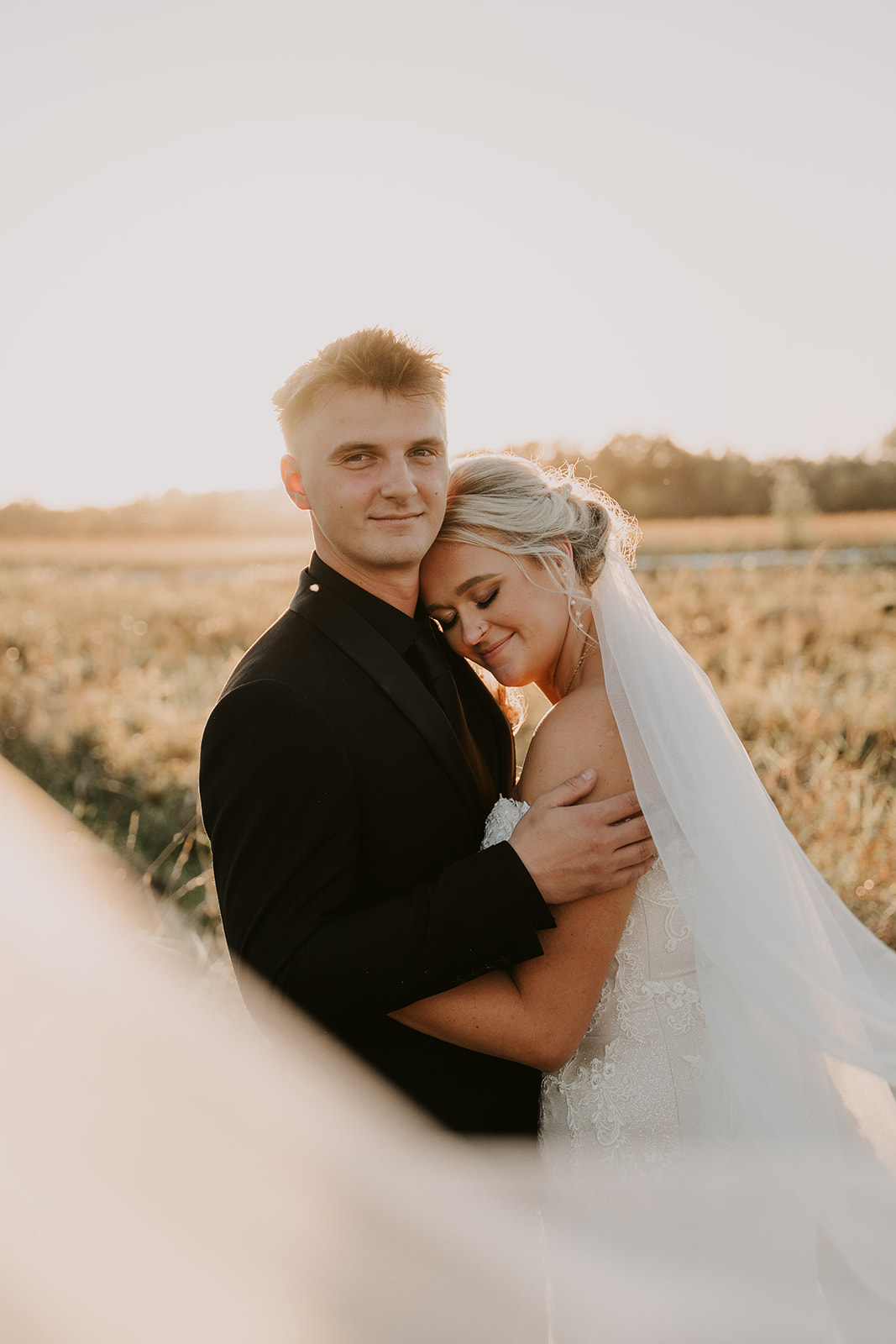 bride and groom during golden hour in field with veil