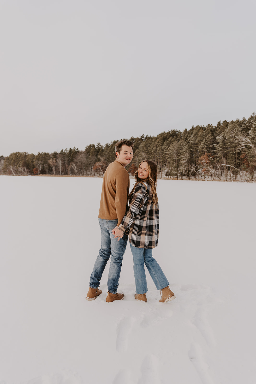 couple smiling for engagement photos on frozen lake