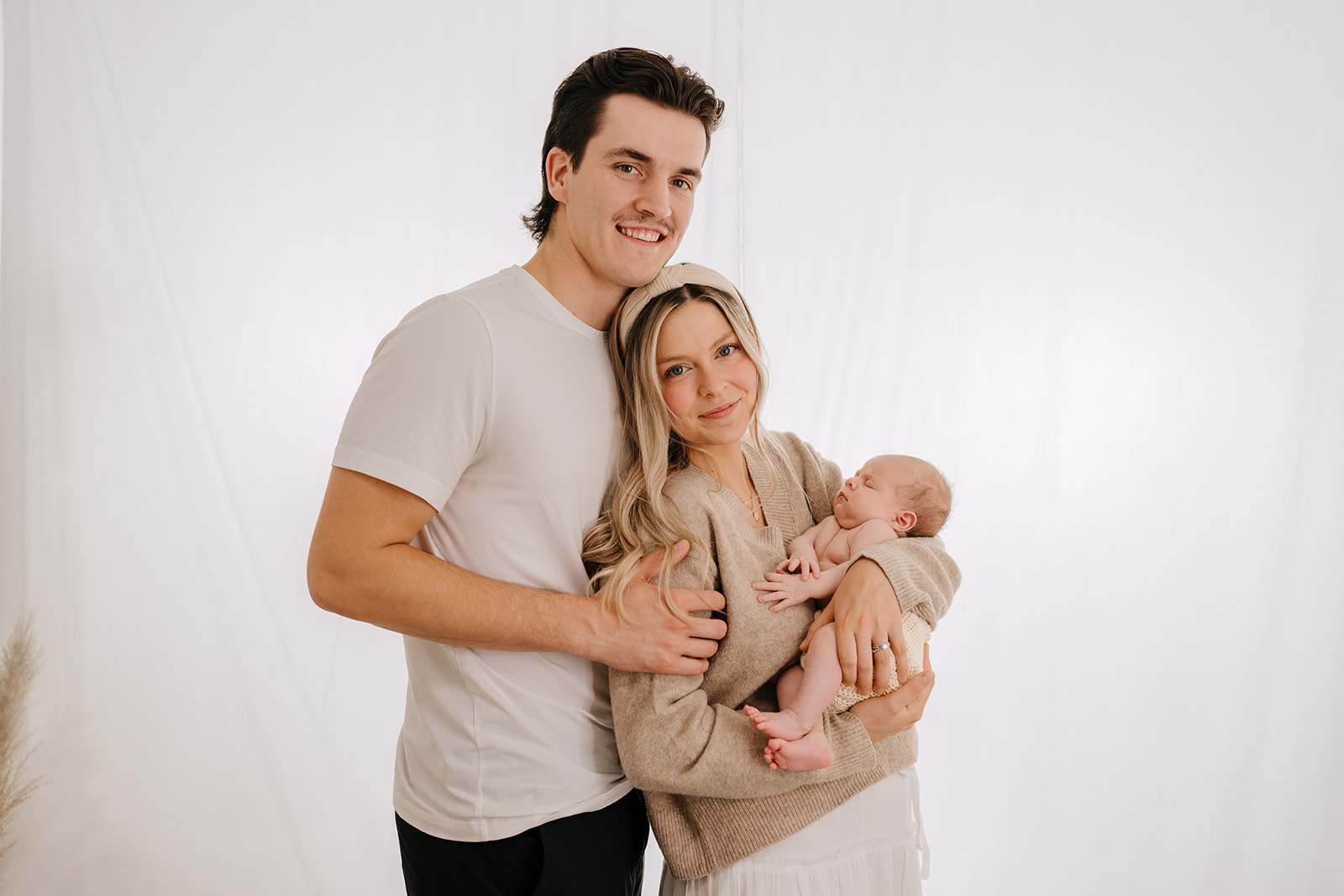 mom and dad holding newborn in white studio